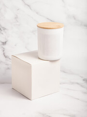 Handmade candle in white cup with wooden lid. Candle and box on marble background