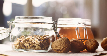 Organic liquid honey in a glass jar next to whole walnuts
