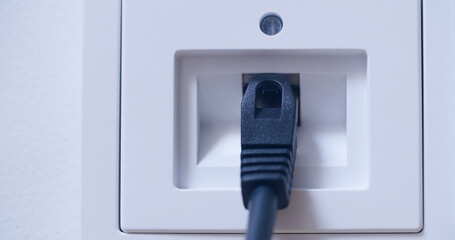 A computer network cable plugged into a wall socket. Closeup shot