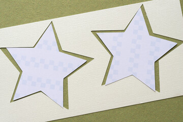 paper stencil with star cutouts and smaller paper stars with cube pattern on rough green paper