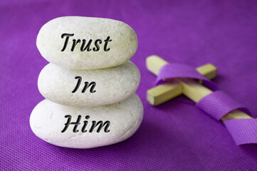 Trust in Him text on stones with Christian cross background. Prayer and Christianity concept