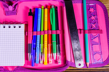 Different school stationeries (pens, pencils, notepad, ruler and protractor) in a pink pencil box....