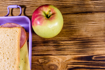 Ripe apple and lunch box with sandwiches on a wooden table. Top view