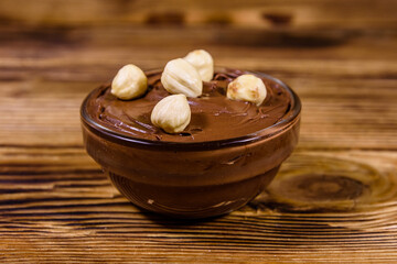Glass bowl with chocolate spread and hazelnuts on a wooden table