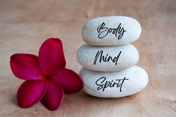 Body, Mind and Soul text engraved on white zen stones with red flower. Meditation and spa concept