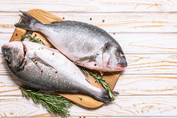 Raw dorado fish with spices and herbs in the cooking pan on white marble background top view, copy space for your design.
