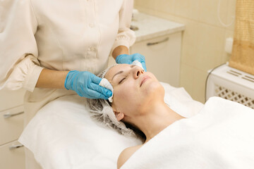 Skin cleansing with cotton pads in the beautician's office. Young woman lies on procedures at the...