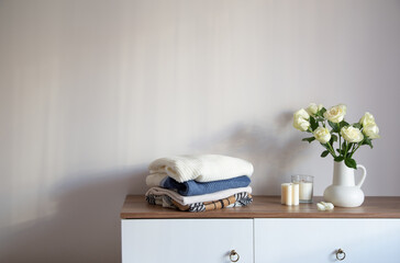 knitted clothing and white roses in jug on modern dresser - obrazy, fototapety, plakaty