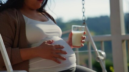 Beautiful pregnant woman drink milk from glass sitting on swing at a rural suburb house. happiness with healthy life at home with dairy nutrition. health of herself and her unborn baby. - Powered by Adobe