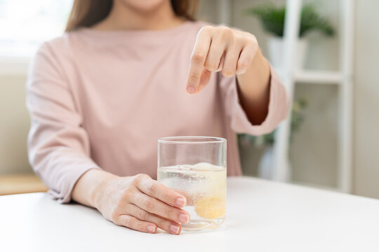 Close up young woman hand putting or dropping effervescent tablet into glass of water, holding pain pill, painkiller medicine, aspirin for treatment, take vitamin c for hangover. Health care concept.