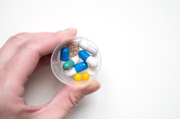Tablets, capsules and granules in a container in a human hand on a light background. Daily dose of...