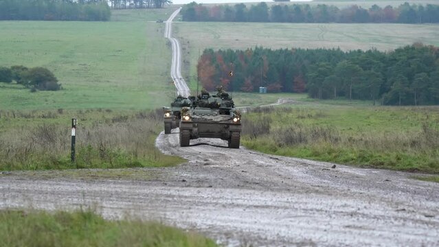 A convoy of four British army Warrior FV510 IFVs moving along a dirt road, in action on a military exercise. Wilts UK