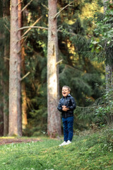 A small lonely boy stands in the forest near the big pine trees and shouts loudly. The child got...