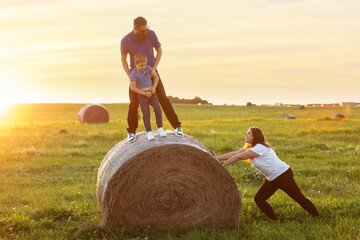 Fun family games on a rural lawn outside in the evening at sunset. A mother pushes a hay roll and...