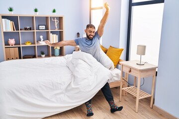 Young hispanic man waking up stretching arms at bedroom