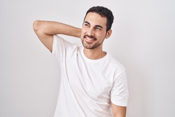 Fototapeta premium Handsome hispanic man standing over white background smiling confident touching hair with hand up gesture, posing attractive and fashionable