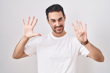 Handsome hispanic man standing over white background showing and pointing up with fingers number...