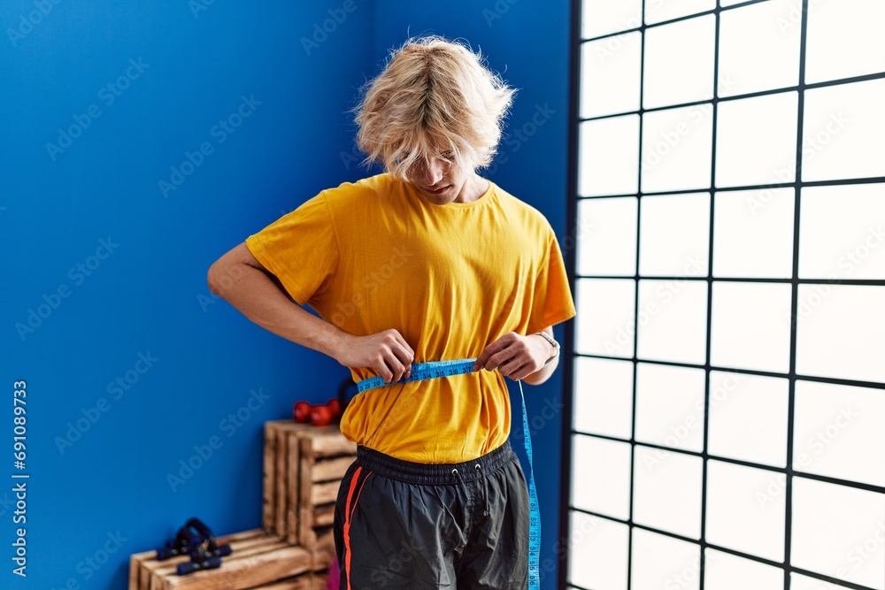 Poster Young blond man measuring waist at sport center