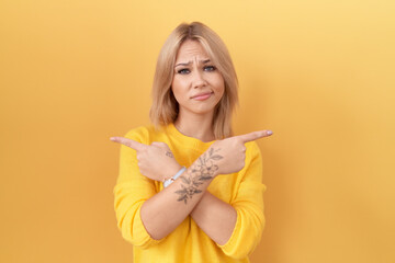 Young caucasian woman wearing yellow sweater pointing to both sides with fingers, different...