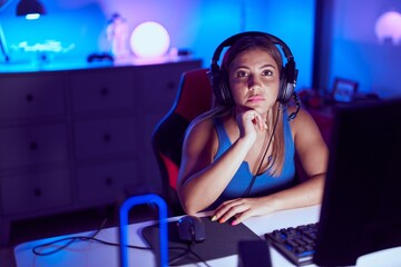 Young beautiful hispanic woman streamer sitting on table with relaxed expression at gaming room