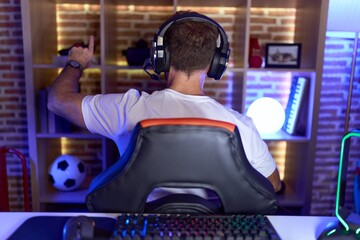 Middle age man with beard playing video games wearing headphones posing backwards pointing ahead...