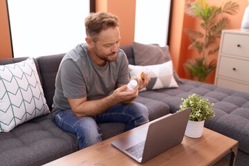 Middle age man using laptop holding pills at home