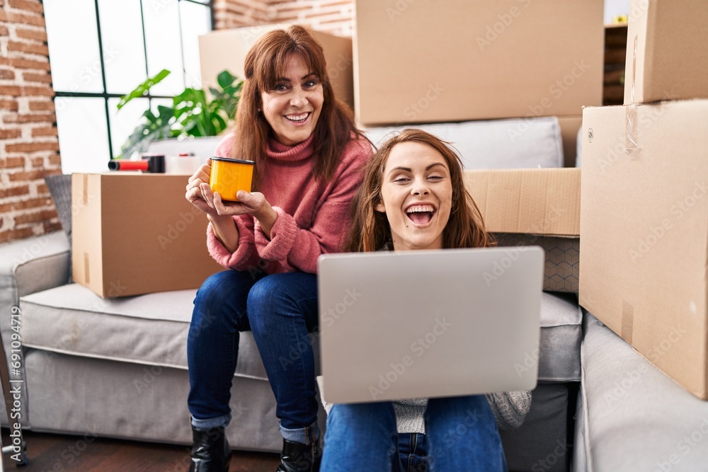 Poster two women mother and daughter using laptop drinking coffee at new home