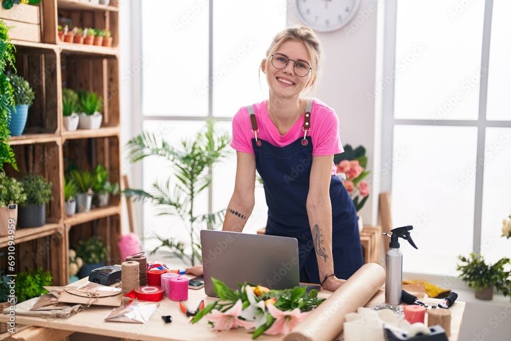 Wall mural Young blonde woman florist smiling confident using laptop at flower shop