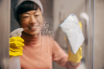 A worthy middle-aged japanese housewife is cleaning window and spraying detergent.