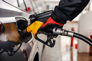 Close up of a hand filling up tank with fuel nozzle at gas station. - obrazy, fototapety, plakaty