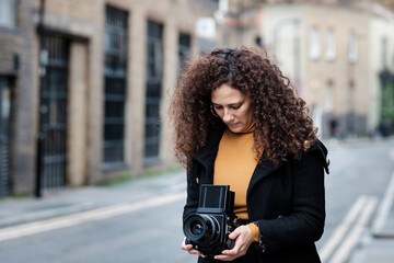 Mature female photographer using medium format analog film camera in the street.