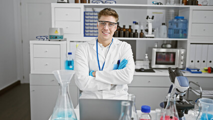 Beaming young caucasian scientist guy, sitting with arms crossed in lab, immersed in high-tech medical research