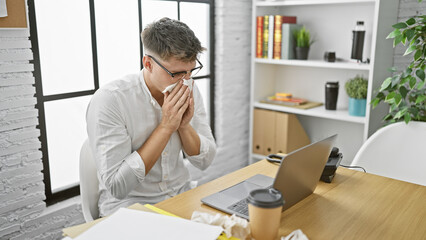 Young, handsome caucasian man, a focused business worker, battling sickness while crunching data on...