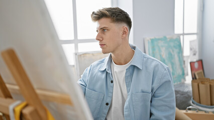 Handsome bearded young caucasian man, an artist, concentrated and immersed in his craft, sits...