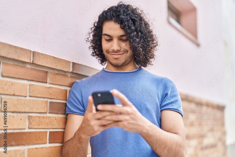 Wall mural Young latin man smiling confident using smartphone at street