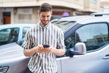 Young caucasian man using smartphone leaning on car at street