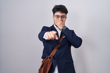 Hispanic man with beard wearing business clothes laughing at you, pointing finger to the camera with hand over mouth, shame expression