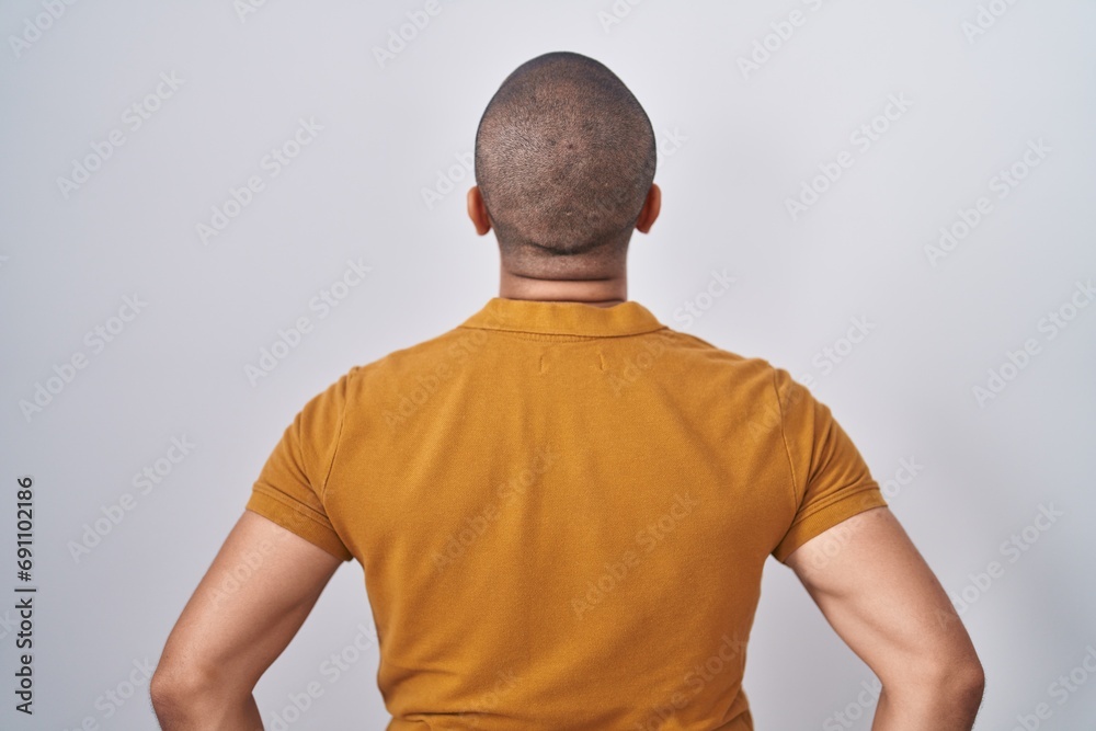 Sticker Hispanic man with beard standing over white background standing backwards looking away with arms on body