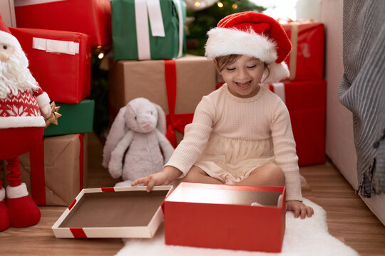 Adorable girl unpacking gift sitting by christmas tree at home