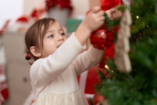 Adorable girl decorating christmas tree standing at home