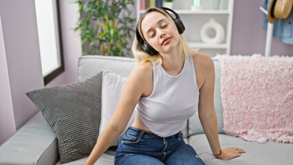 Fototapeta premium Young blonde woman listening to music relaxed on sofa at home