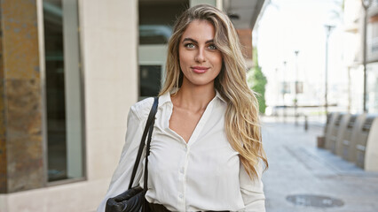 Radiant young blonde woman, exuding confidence with a sparkling smile, stands outdoors on a sunny city street, enjoying the urban ambiance and spreading positive vibes.