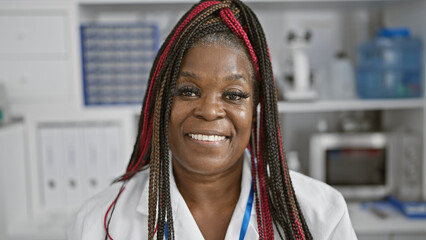 Confident african american woman scientist with braids, smiling beautifully in busy analytics...