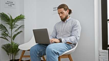 Young hispanic man using laptop sitting on chair at waiting room