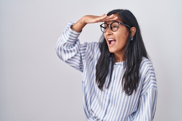 Young hispanic woman wearing glasses very happy and smiling looking far away with hand over head. searching concept. - obrazy, fototapety, plakaty
