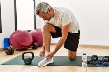 Middle age grey-haired man tying shoe at sport center