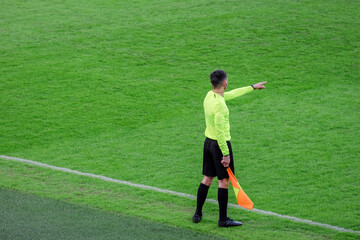 The line referee on the edge of the field with a flag in his hand indicates offside with his hand