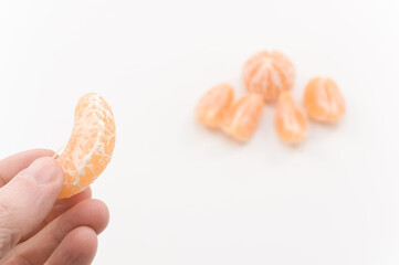 immagine con primo piano di mano che regge spicchio di frutto di mandarino, clementina su superficie bianca