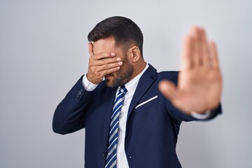 Handsome hispanic man wearing suit and tie covering eyes with hands and doing stop gesture with sad and fear expression. embarrassed and negative concept.