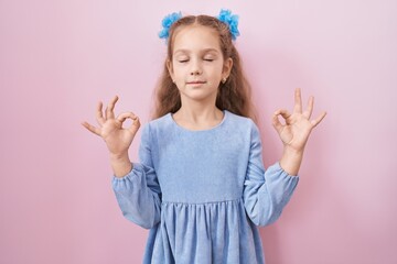 Young little girl standing over pink background relax and smiling with eyes closed doing meditation gesture with fingers. yoga concept.